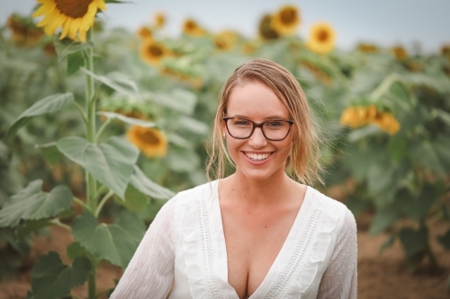 Young adult woman sitting in sunflower field - Australian Stock Image