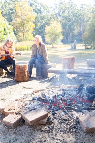 Young adults sitting around campfire in the morning - Australian Stock Image