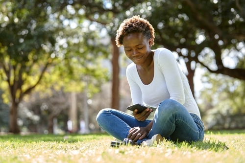 Young African woman enjoying time in sunshine on mobile phone - Australian Stock Image