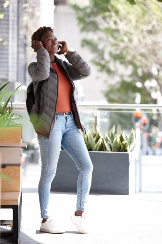 Young African woman listening to music wearing wireless headphones in city - Australian Stock Image
