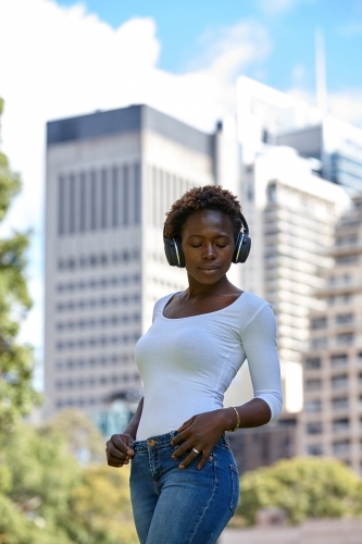 Young African woman listening to music wearing wireless headphones in city - Australian Stock Image