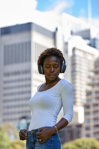 Young African woman listening to music wearing wireless headphones in city - Australian Stock Image