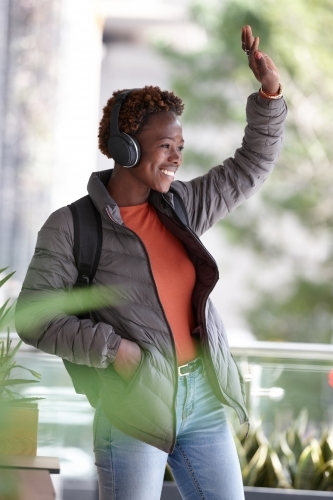 Young African woman listening to music wearing wireless headphones waving - Australian Stock Image
