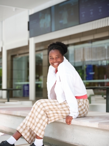 Young African woman sitting in university courtyard - Australian Stock Image