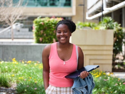 Young African woman standing with laptop in university courtyard - Australian Stock Image