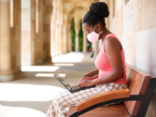 Young African woman wearing a mask at a university campus - Australian Stock Image