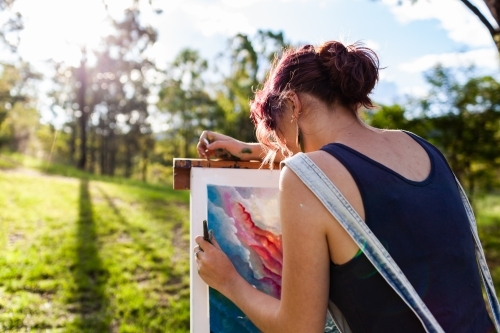 Young artist in overalls painting art outside in nature - Australian Stock Image