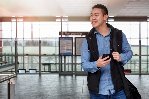 Young Asian commuter holding phone walking out from train station - Australian Stock Image