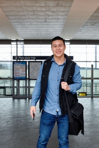 Young Asian commuter waiting at train station entrance - Australian Stock Image