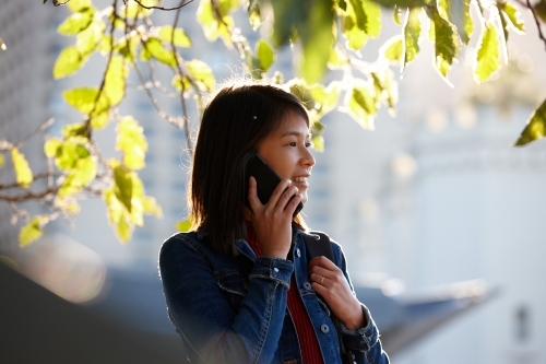 Young Asian female talking on mobile phone under tree