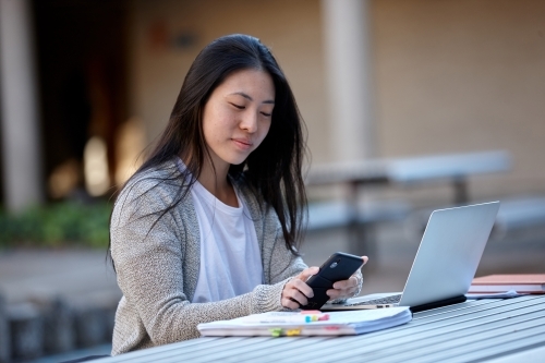 Young Asian female university student studying on laptop outdoors - Australian Stock Image