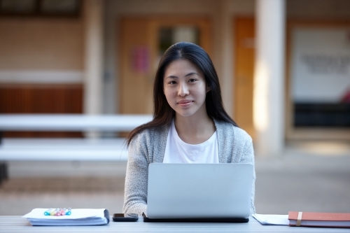 Young Asian female university student studying on laptop outdoors - Australian Stock Image