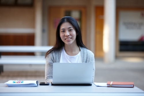 Young Asian female university student studying on laptop outdoors - Australian Stock Image