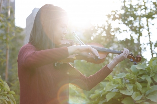 Young Asian female violin player practising outdoors - Australian Stock Image