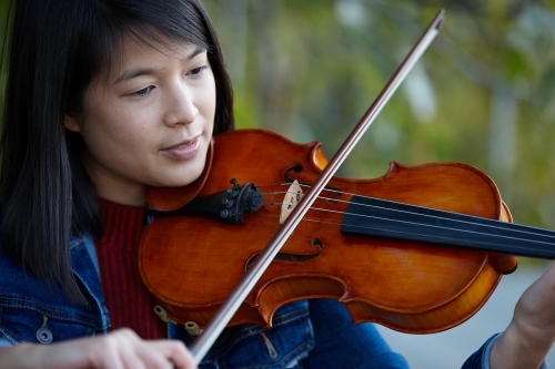 Young Asian female violin player practising outdoors - Australian Stock Image