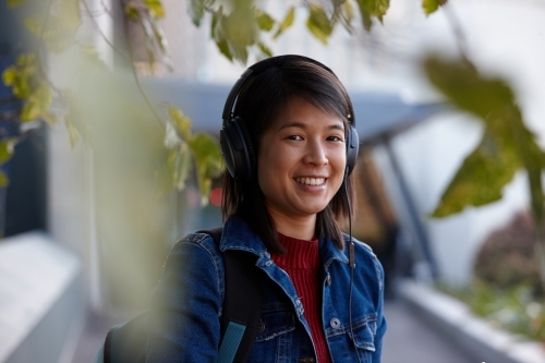 Young Asian female with headphones under tree - Australian Stock Image