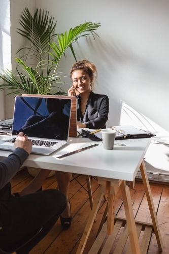 Young asian girl on the phone working opposite a colleague - Australian Stock Image