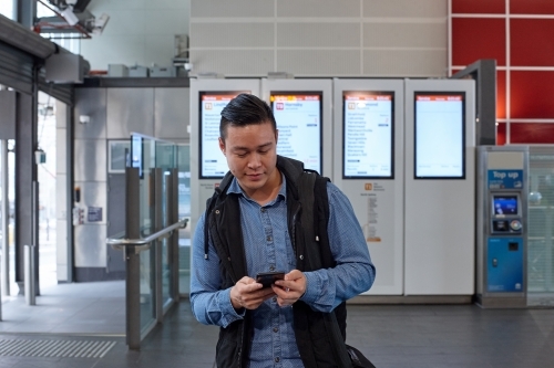Young Asian man checking mobile device at train station - Australian Stock Image