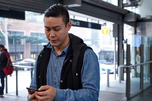Young Asian man checking mobile device at train station - Australian Stock Image