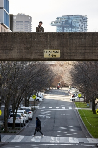 Young Asian man standing on bridge with city in background - Australian Stock Image
