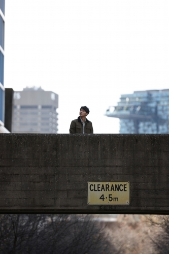 Young Asian man standing on bridge with city in background