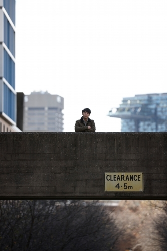 Young Asian man standing on bridge with city in background - Australian Stock Image