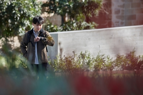 Young Asian university student standing on-campus checking smart watch - Australian Stock Image