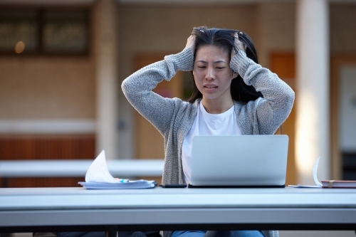 Young Asian university student studying on laptop outdoors stressed - Australian Stock Image