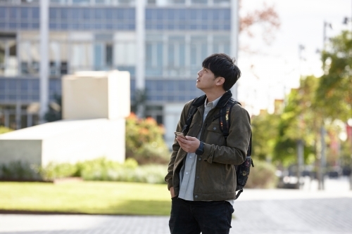 Young Asian university student using mobile phone on-campus - Australian Stock Image