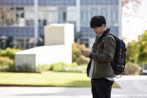 Young Asian university student using mobile phone on-campus - Australian Stock Image