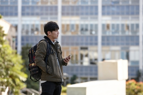 Young Asian university student using mobile phone on-campus - Australian Stock Image