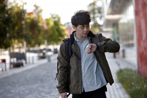 Young Asian university student walking on-campus checking smart watch - Australian Stock Image