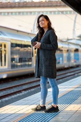 Young Asian woman waiting at train station with mobile phone - Australian Stock Image
