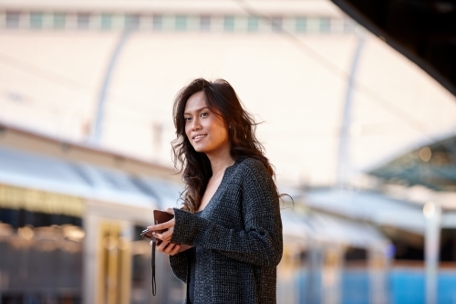 Young Asian woman waiting at train station with mobile phone - Australian Stock Image