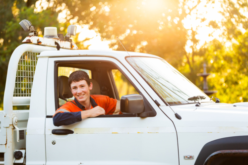 Young Aussie teenager driving ute on Australian farm wearing high-vis workwear in golden light - Australian Stock Image