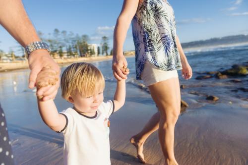 Young blonde boy holding his mum and dads hands at the beach