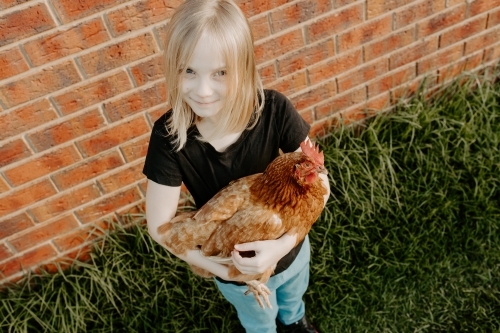Young blonde girl holding her pet chicken outdoors - Australian Stock Image