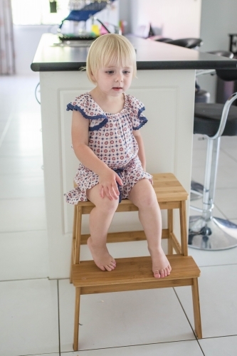 Young blonde girl sitting on step chair in kitchen at home - Australian Stock Image