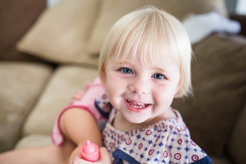 Young blonde girl smiling holding toys at home - Australian Stock Image