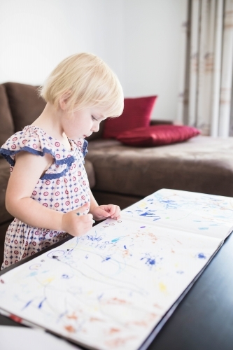 Young blonde girl standing at table colouring in with crayons - Australian Stock Image