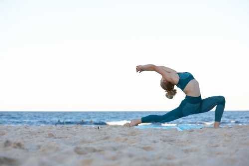 Young blonde-haired woman at beach doing yoga
