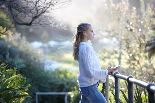 Young blonde-haired woman listening to music with earphones outdoors - Australian Stock Image