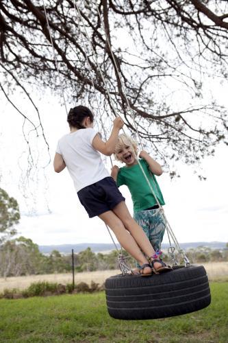 Young boy and girl on a tyre swing in a country backyard