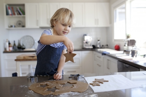 Young boy baking gingerbread cookies in kitchen at home - Australian Stock Image