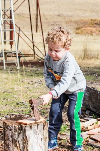 Young boy chopping wood with axe on farm - Australian Stock Image