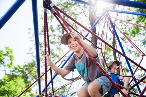 Young boy climbing spiderweb playground equipment at park