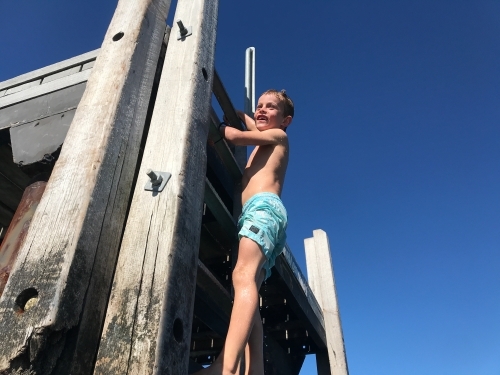 Young boy climbing up ladder of a jetty on a river - Australian Stock Image