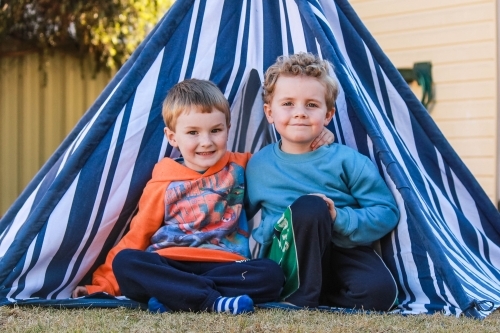 Young boy cousins with arms around each other sitting in teepee tent - Australian Stock Image