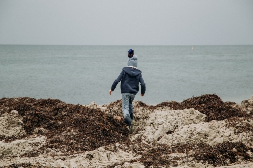 Young boy exploring coastal beach on cold winter day - Australian Stock Image