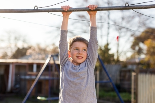 Young boy hanging from washing line in backyard - Australian Stock Image